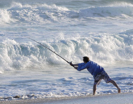 fisherman casting off into wild surf