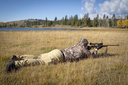 A Hunter In Camouflage Prone Aiming a Rifle