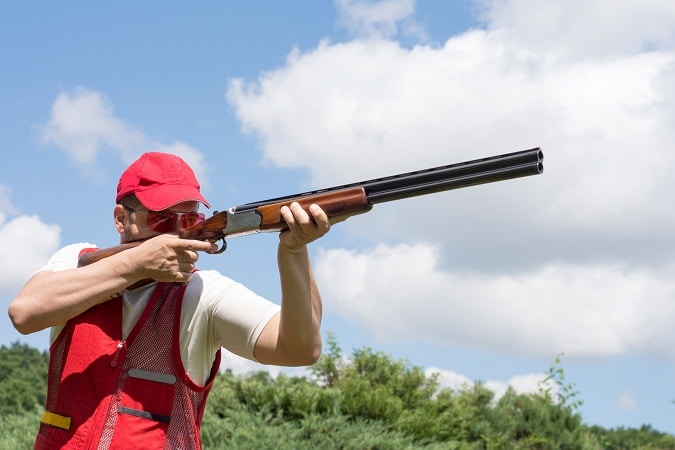 Man shooting skeet with a shotgun and best shooting vest