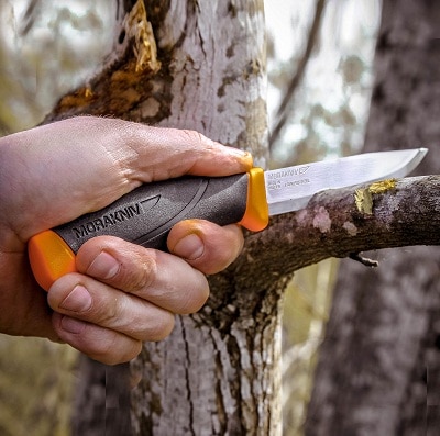 man cutting tree branch with survival knife