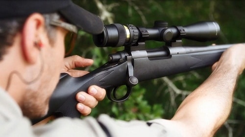 man aiming rifle looking through a scope