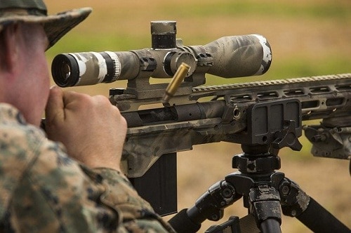 man looking through scope after firing rifle