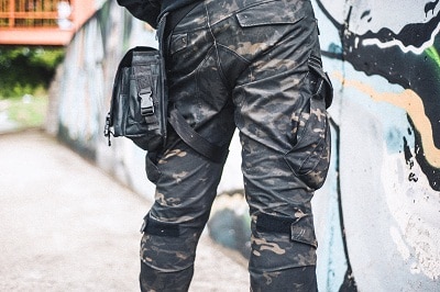An urban man in a camouflage military pants stands next to the wall.