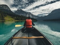 Young Man Canoeing on lake in the rocky mountains with canoe and life vest