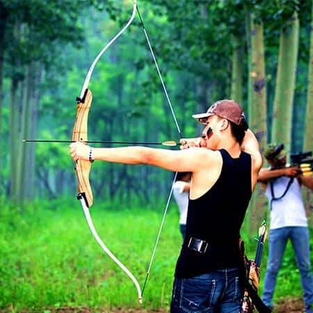 man aiming arrow with recurve bow in woods
