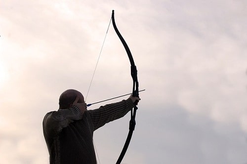 man aiming arrow with recurve bow