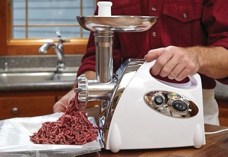 man grinding meat with electric grinder in the kitchen