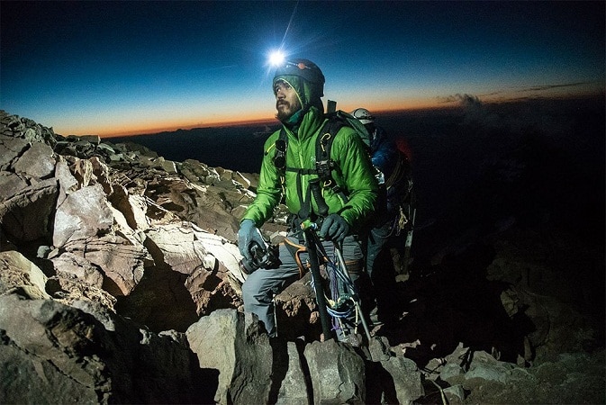 man hiking a rocky mountain at dawn with a headlamp