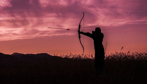 man shooting arrow with longbow at dawn