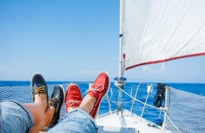 Two pairs legs in red and blue topsiders on white yacht deck