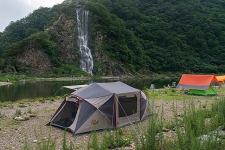 family tent pitched near a small waterfall