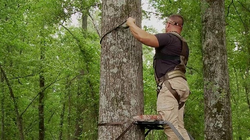 hunter with harness setting up treestand
