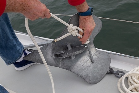man hands tying anchor on boat ledge