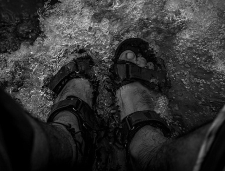 man's feet wearing sandals submerged in water