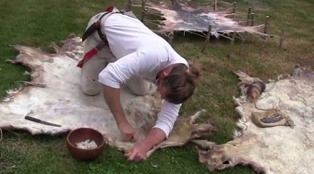 Woman removing deer fur with a scraper on the ground