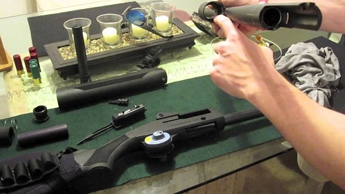 man wiping clean disassembled rifle on table