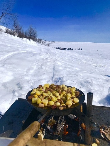 potatoes and meat on pan cooked with wood in a snowy landscape