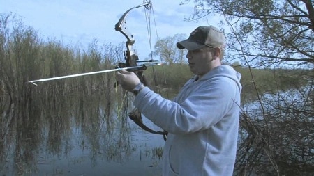 bowfisher fixing arrow in a shruby lake