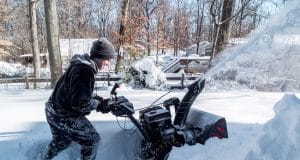 boy plowing driveway with snowblower in winter