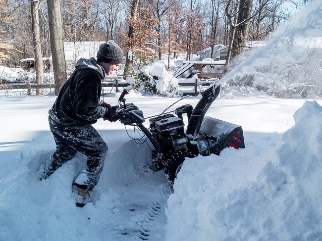 boy plowing driveway with snowblower in winter