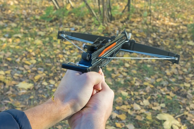 hands aiming crossbow pistol in the field