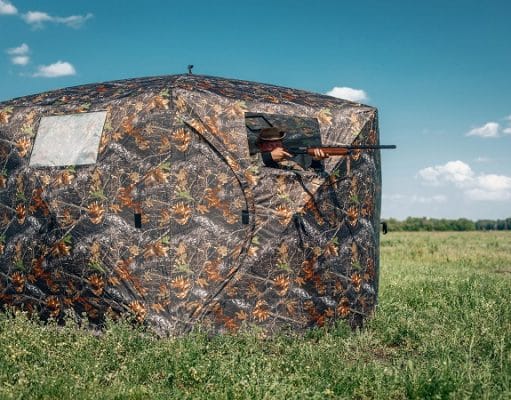 hunter aiming rifle from a ground blind