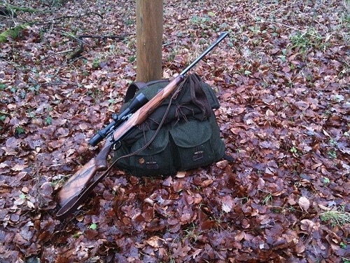 Hunting rifle on bag on leafy ground