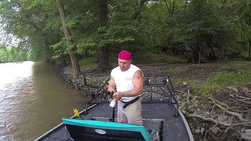 Man in a boat by the river setting up for bowfishing
