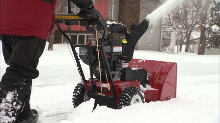 man removing snow from sidewalk with snowblower