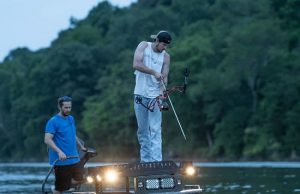 men bowfishing in the lake at dawn
