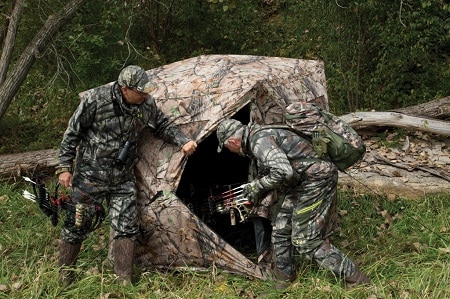 two bow hunters looking inside a ground blind
