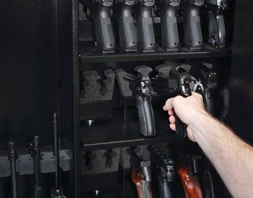 hand getting pistol from a selection of guns in safe