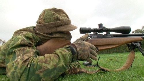 hunter aiming rifle with scope on the grassy ground