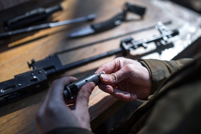 man hands cleaning rifle parts on table