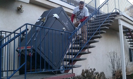 man pulling a gun safe up the stairs