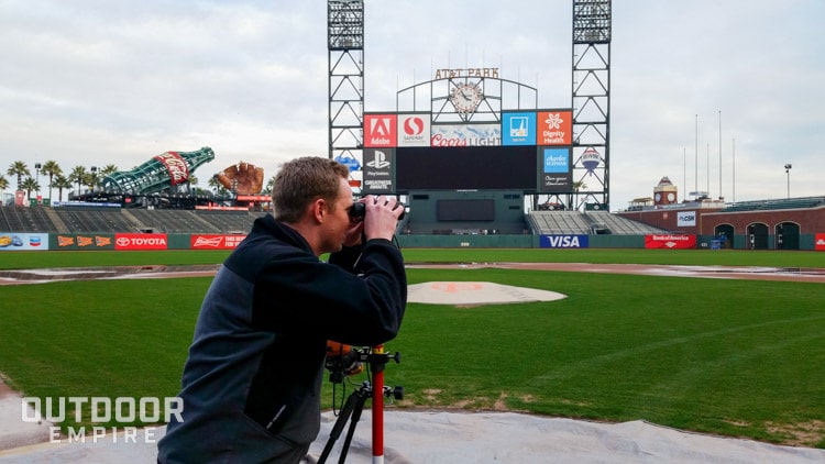 Man surveying baseball field with rangefinder on tripod