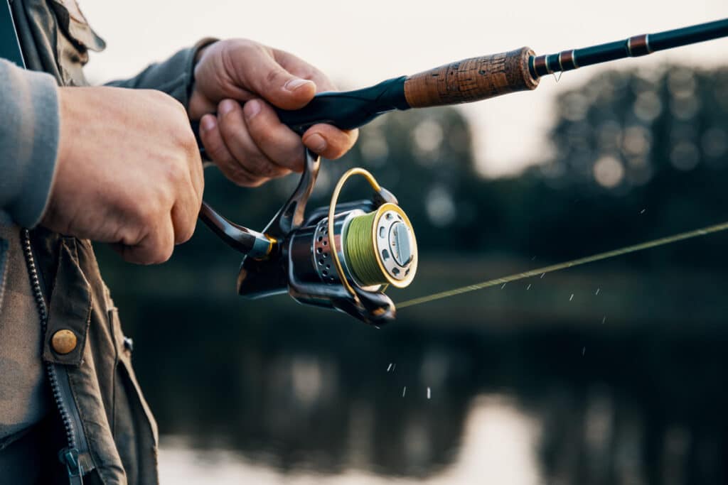 man holding spincasting reel on a lake