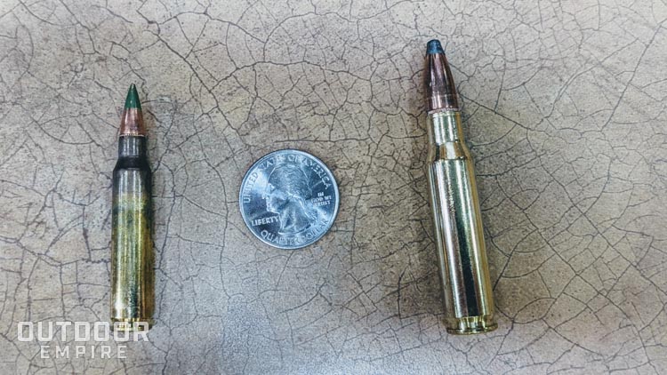 A 5. 56mm cartridge next to a. 308 cartridge with a quarter for scale