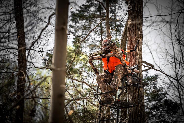 Man aiming rifle while sitting in a treestand
