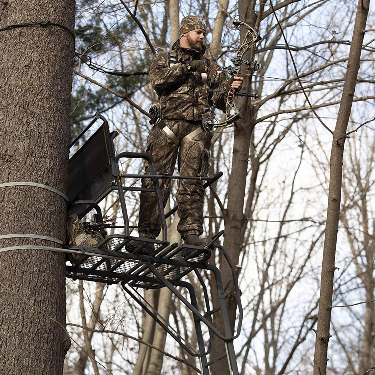 Man in camo standing on a treestand with a bow in hand