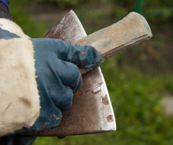 A man in gloves sharpens an iron axe with a whetstone