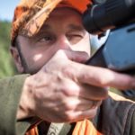 Hunter in orange hat aiming rifle
