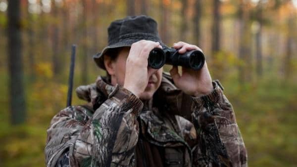 Hunter with rifle looking into binoculars