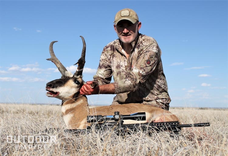 Hunter holding up antelope head with rifle laying in front