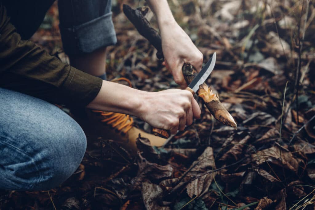 Woman shaving tree branch with a knife