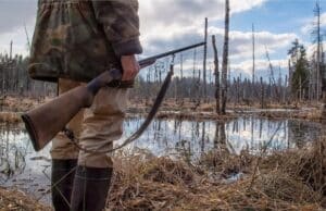 hunter holding rifle by a swamp