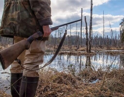 hunter holding rifle by a swamp