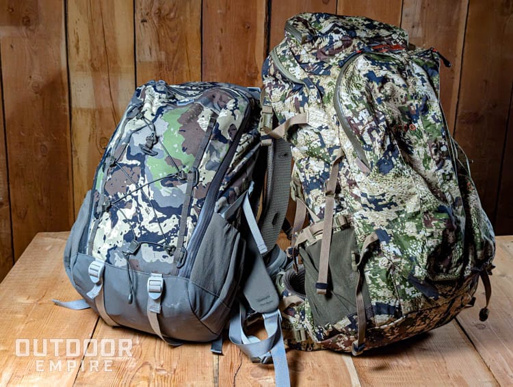 A hunting daypack and a bigger hunting backpack next to each other on a wood table