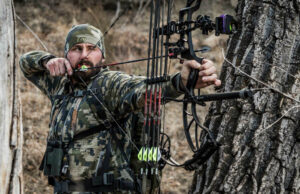 Hunter in camo drawing bow and aiming for clean shot behind a tree