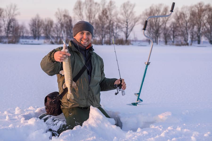 Winter fishing concept. Fisherman in action with trophy in hand. Catching pike fish from snowy ice at lake.
